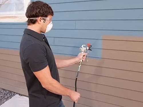 Technician in a respirator spraying an even coat from a compressor-fed spray gun