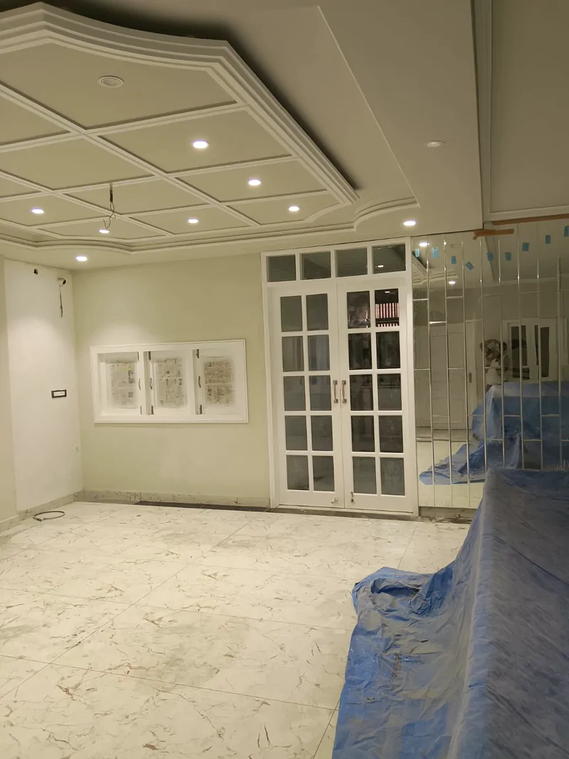 Room with a coffered POP ceiling, recessed lights, glazed doors and a mirrored panel wall, floor protected with blue sheeting