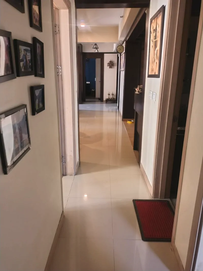 Apartment hallway with cream walls, framed pictures and dark timber door frames, looking through to the rooms beyond